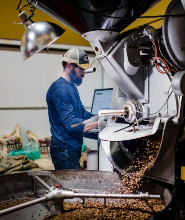 Man behind a coffee roasting machine with roasted coffee spilling out